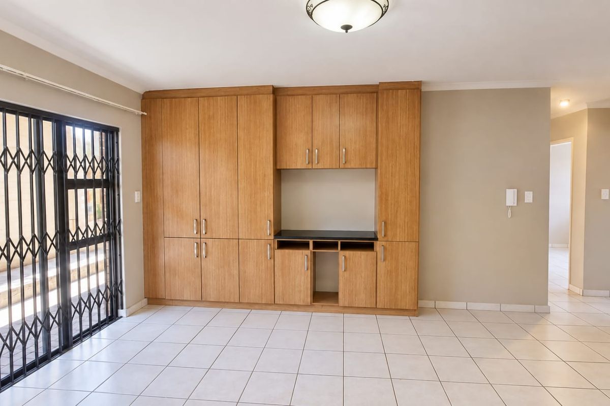 Spacious living area featuring neutral tiled flooring, extensive built-in wooden cabinetry, and a secure sliding door access to the exterior.