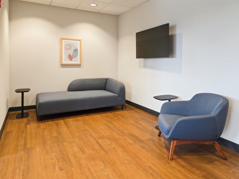 A modern office waiting area featuring wood-look flooring, recessed ceiling lighting, and a wall-mounted television.