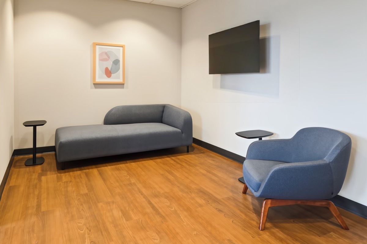 A modern office waiting area featuring wood-look flooring, recessed ceiling lighting, and a wall-mounted television.