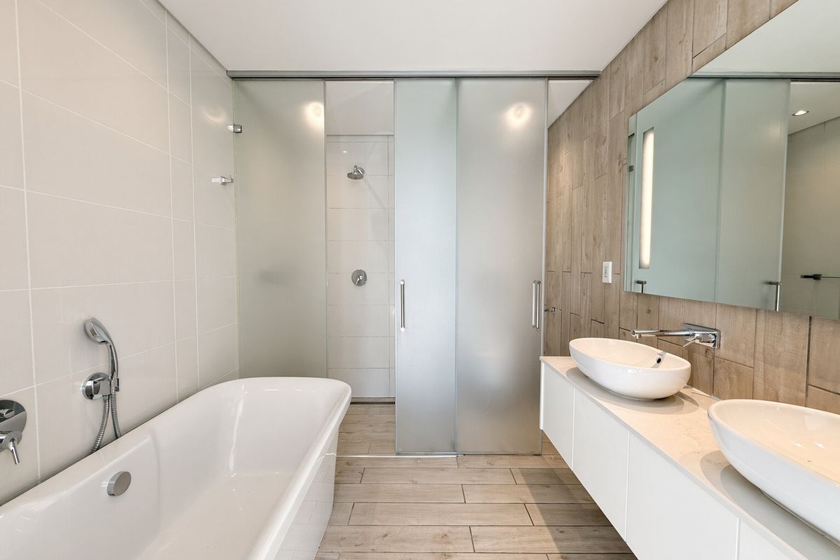Modern bathroom featuring a freestanding bathtub, double vanity with vessel sinks, and a spacious walk-in shower with frosted glass sliding doors.