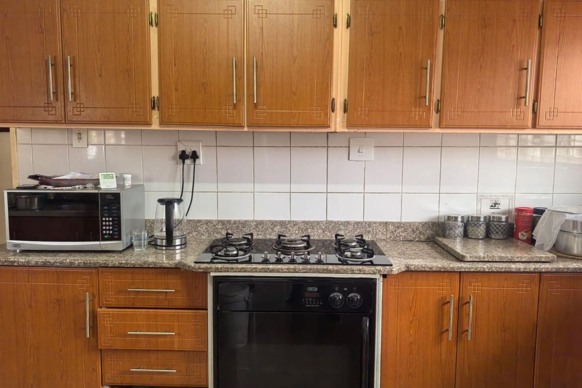 A functional kitchen featuring wood-look laminate cabinetry, granite countertops, a ceramic tile backsplash, and a built-in gas hob with an oven.