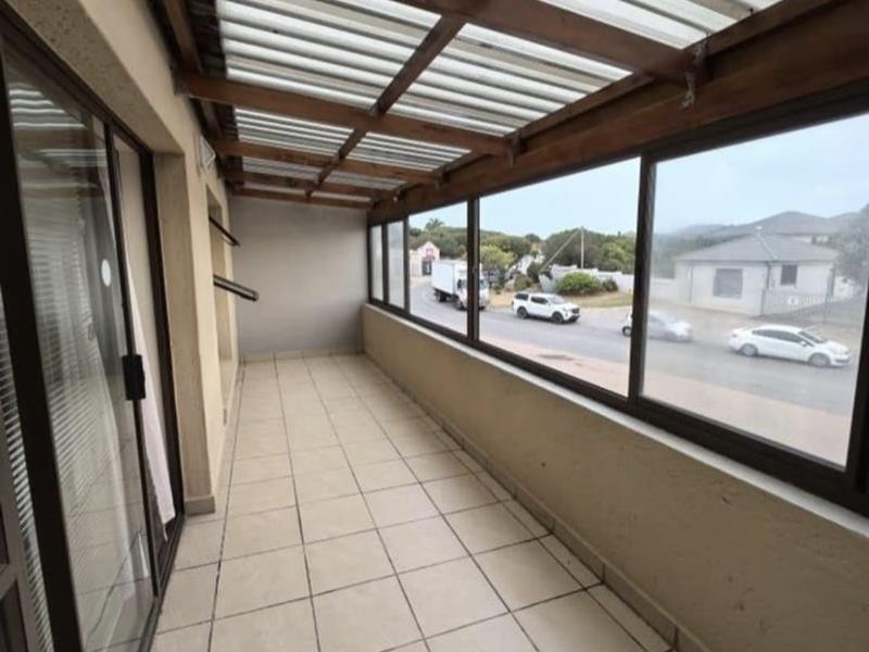 A covered balcony featuring tiled flooring, a timber pergola roof with translucent sheeting, and large sliding glass doors providing access to the apartment.