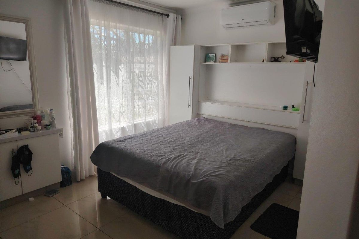 A well-lit bedroom featuring tiled flooring, built-in cabinetry with integrated shelving, and a wall-mounted air conditioning unit.