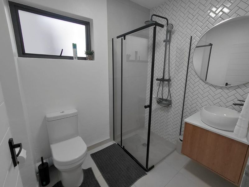 Modern bathroom featuring a walk-in shower with black-framed glass, herringbone tiled feature wall, vessel sink on a floating vanity, and a toilet.