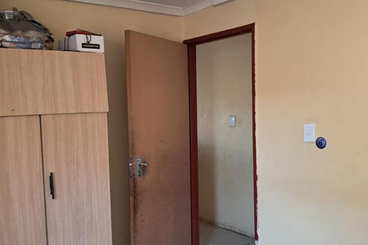 A bedroom featuring tiled flooring, a built-in wardrobe, and visible ceiling water staining, requiring cosmetic updates to improve the overall condition.