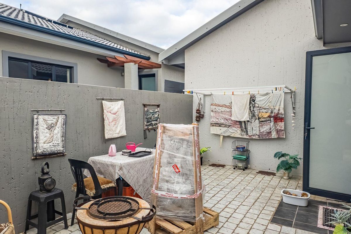 A private rear courtyard featuring paved flooring, textured concrete boundary walls, and a wall-mounted drying rack, providing a functional outdoor utility space.