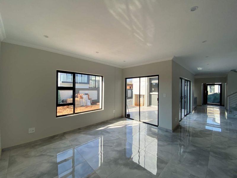 Spacious open-plan living area featuring polished porcelain tiles, modern aluminium sliding doors, and recessed downlighting, offering a bright and contemporary blank canvas.