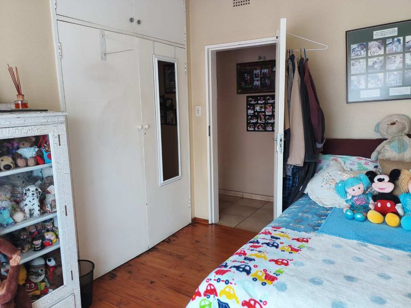 A bedroom featuring wooden flooring and built-in cupboards with overhead storage, providing functional storage space and access to an adjoining room.