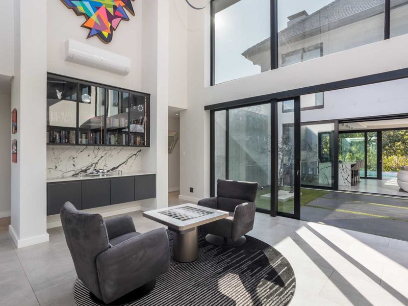 Spacious double-volume living area featuring floor-to-ceiling glass doors, built-in cabinetry with marble detailing, and seamless access to the outdoor patio.