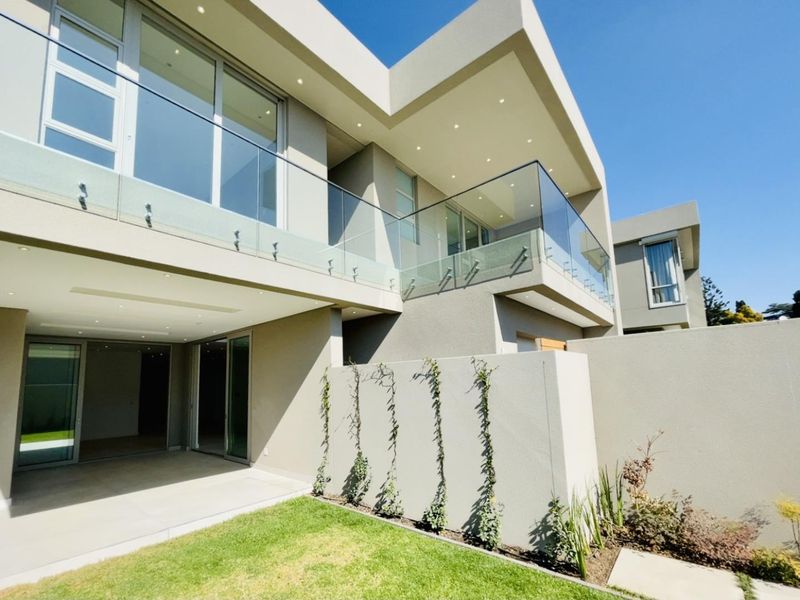 Modern double-story cluster home featuring a covered patio, glass balustrades, recessed lighting, and a well-maintained garden area.