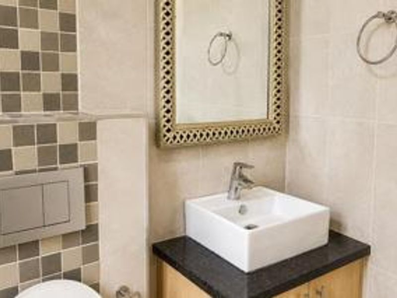 A modern bathroom featuring a vessel sink on a vanity cabinet, wall-mounted toilet flush plate, and decorative tiled wall accents.