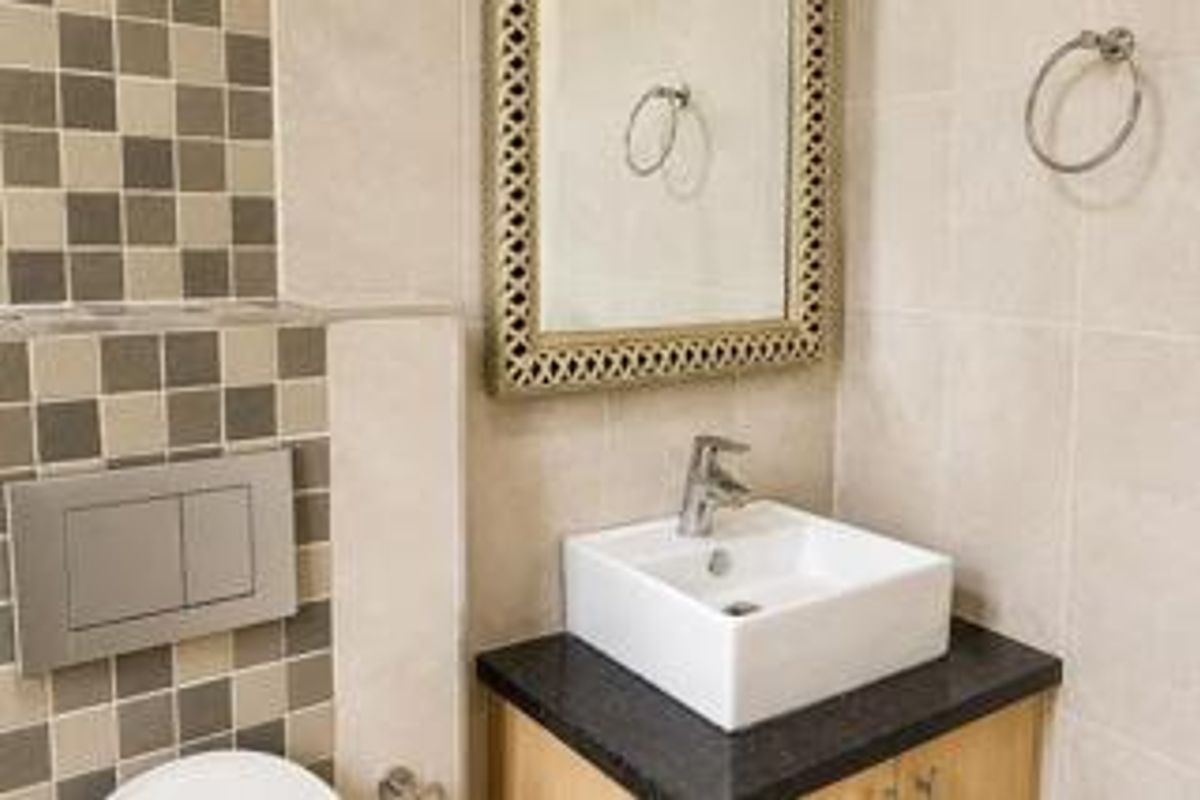 A modern bathroom featuring a vessel sink on a vanity cabinet, wall-mounted toilet flush plate, and decorative tiled wall accents.