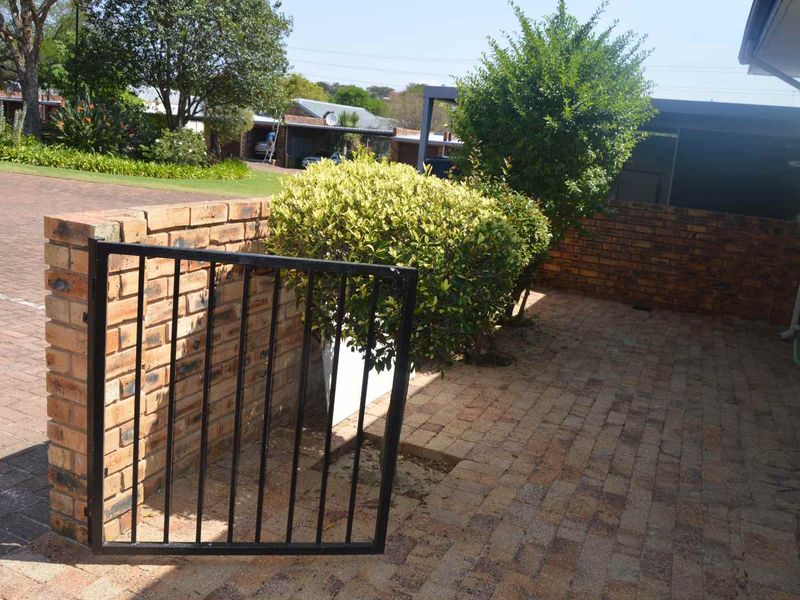 A paved front entrance area featuring a brick boundary wall and a metal gate, providing access to the townhouse exterior.