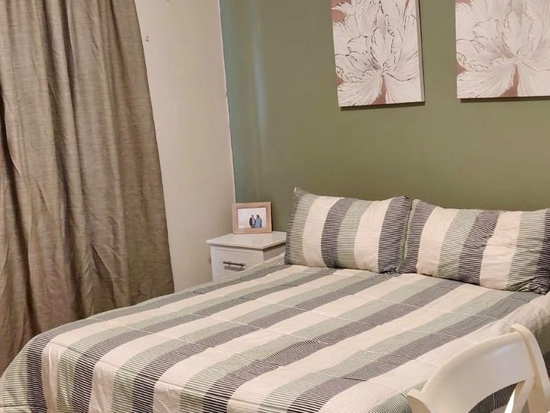 A bedroom featuring tiled flooring and a green accent wall, providing a functional and neutral sleeping space.