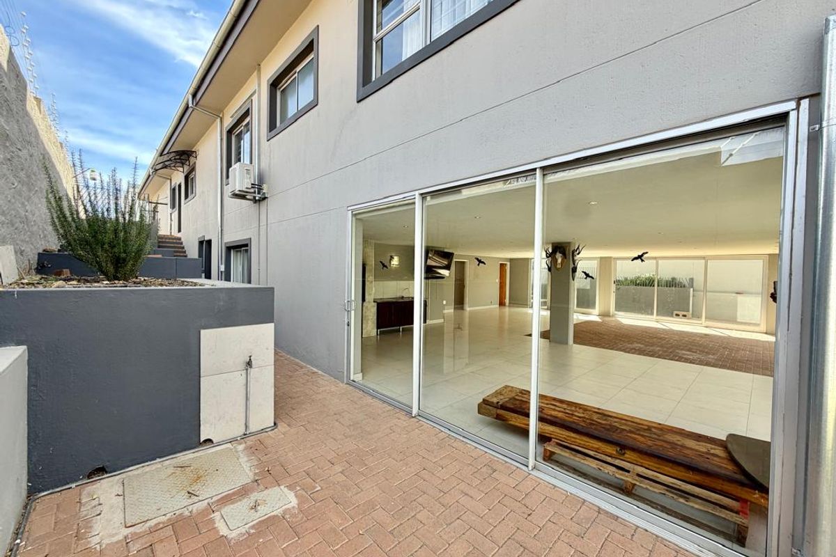 Rear exterior view featuring a paved patio area, large sliding glass doors providing access to the interior, and a modern retaining wall structure.