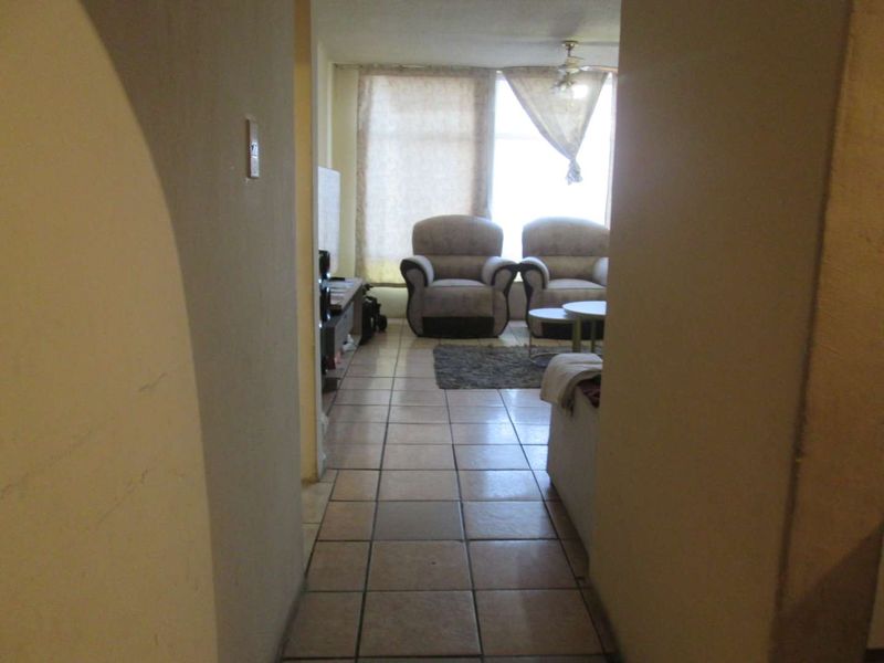 A view from a hallway into a living room featuring ceramic floor tiles and a ceiling fan, requiring cosmetic updates to improve the space.