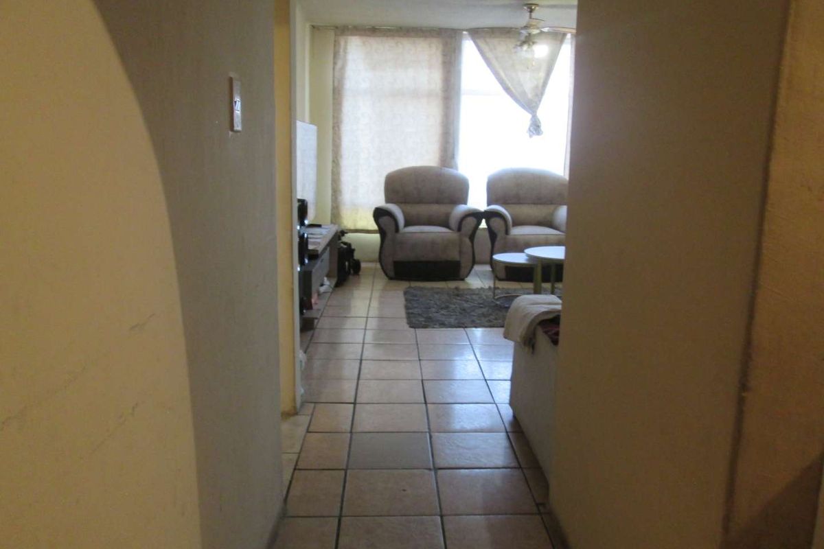 A view from a hallway into a living room featuring ceramic floor tiles and a ceiling fan, requiring cosmetic updates to improve the space.