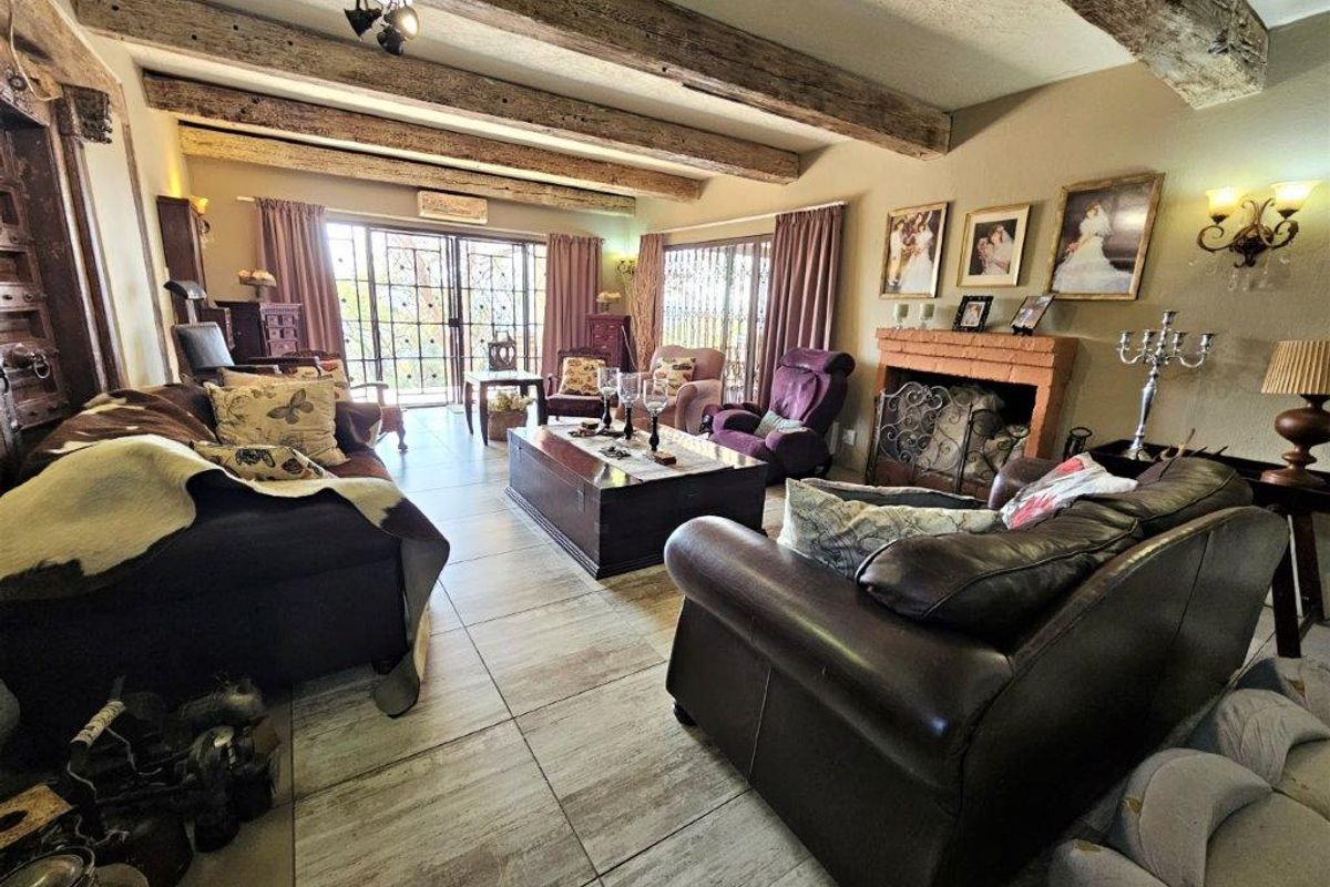 Spacious living room featuring exposed timber ceiling beams, tiled flooring, and a traditional brick fireplace, with large sliding doors leading to the outdoor area.