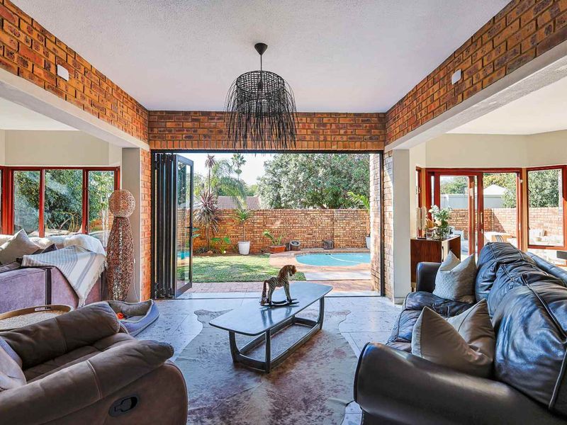 Spacious open-plan living area featuring exposed brick walls, large bi-fold doors opening to the garden and pool, and modern tiled flooring.