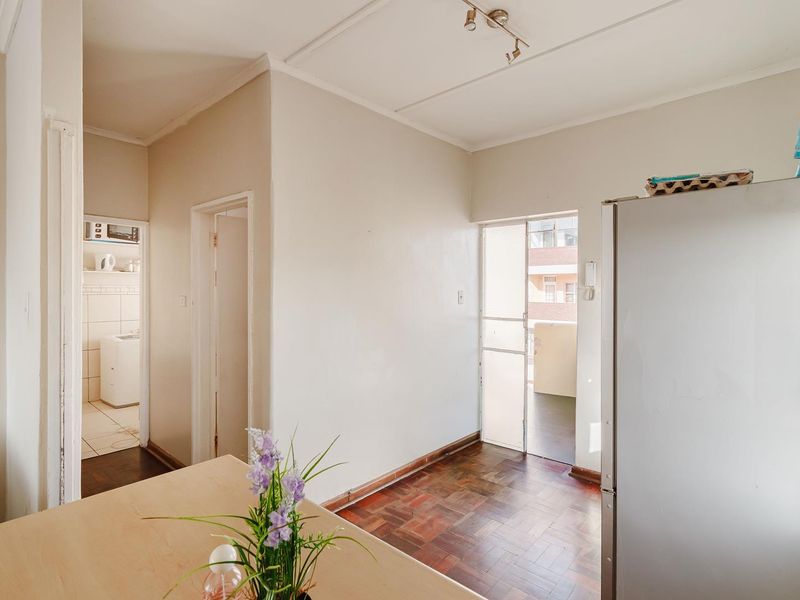 Open plan living area featuring parquet flooring, neutral wall tones, and direct access to an adjacent balcony and utility space.