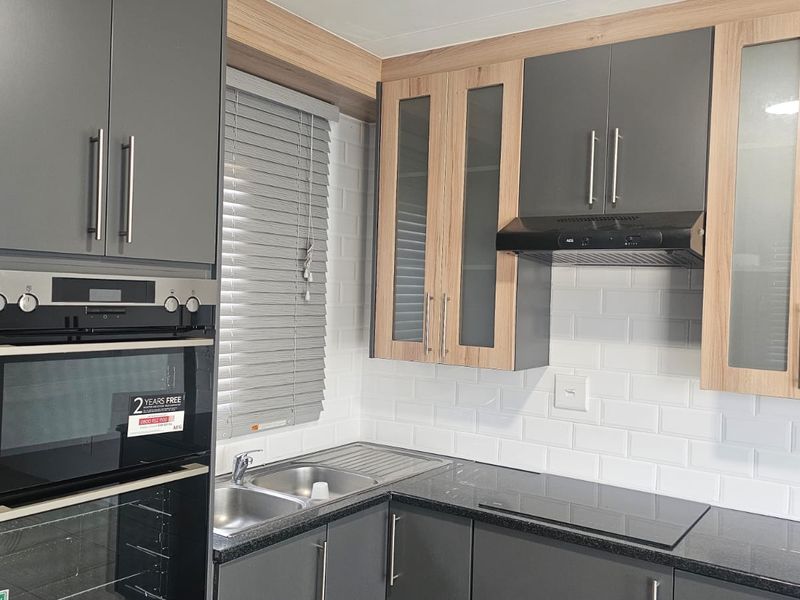 Modern kitchen featuring grey and wood-tone cabinetry, stone countertops, subway tile backsplash, and integrated appliances including an oven and hob.