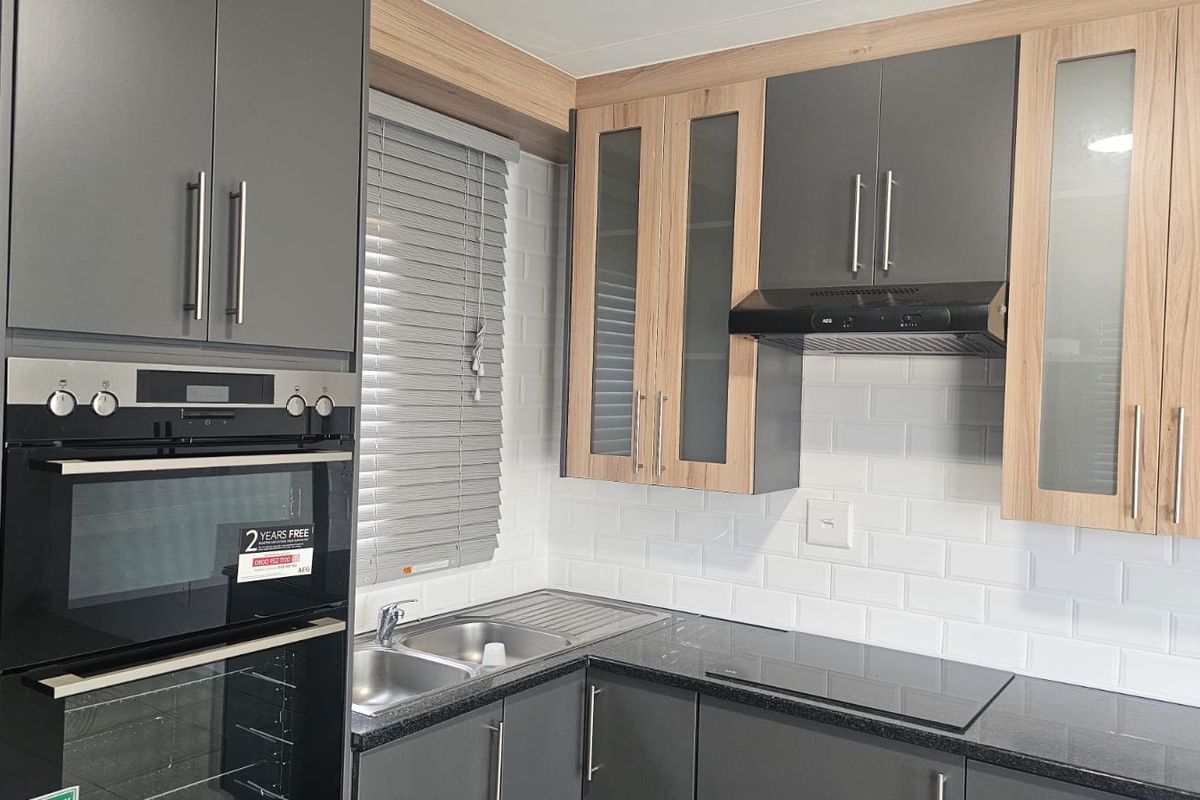 Modern kitchen featuring grey and wood-tone cabinetry, stone countertops, subway tile backsplash, and integrated appliances including an oven and hob.