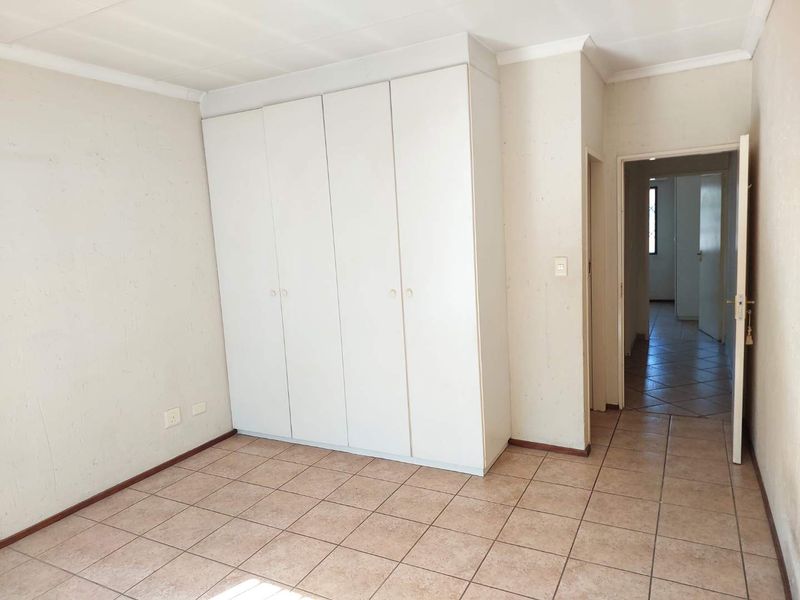 An empty bedroom featuring built-in cupboards, tiled flooring, and a coved ceiling, offering a blank canvas for personalization.
