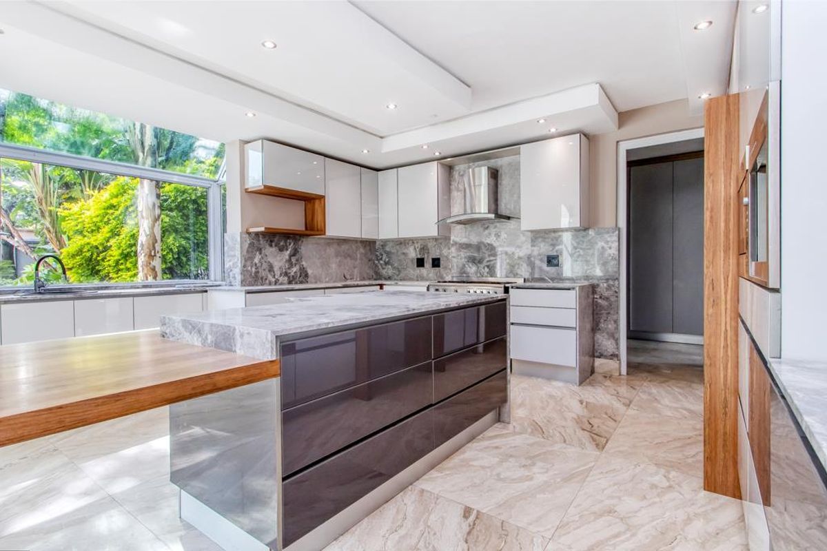Modern kitchen featuring a large central island with stone countertop, high-gloss cabinetry, integrated appliances, and large windows overlooking the garden.