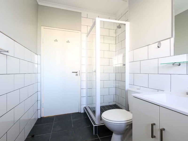 A clean, modern bathroom featuring a glass-enclosed shower, white subway-style wall tiles, dark floor tiles, and a vanity unit with a basin.