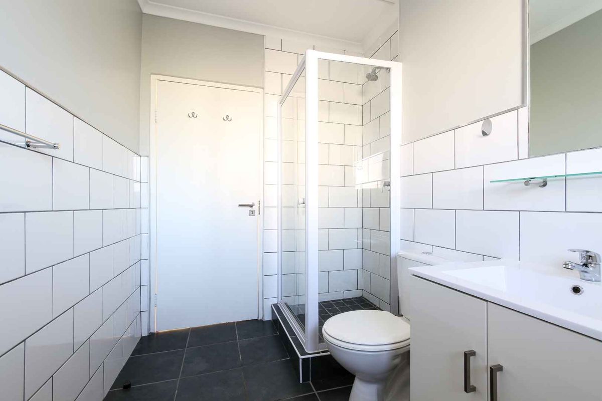 A clean, modern bathroom featuring a glass-enclosed shower, white subway-style wall tiles, dark floor tiles, and a vanity unit with a basin.