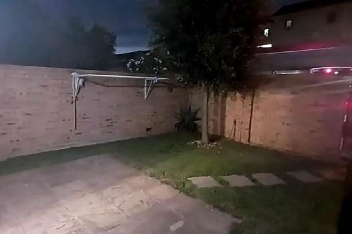 A private rear garden area featuring a brick boundary wall, paved patio section, small lawn, and a wall-mounted clothes drying rack.