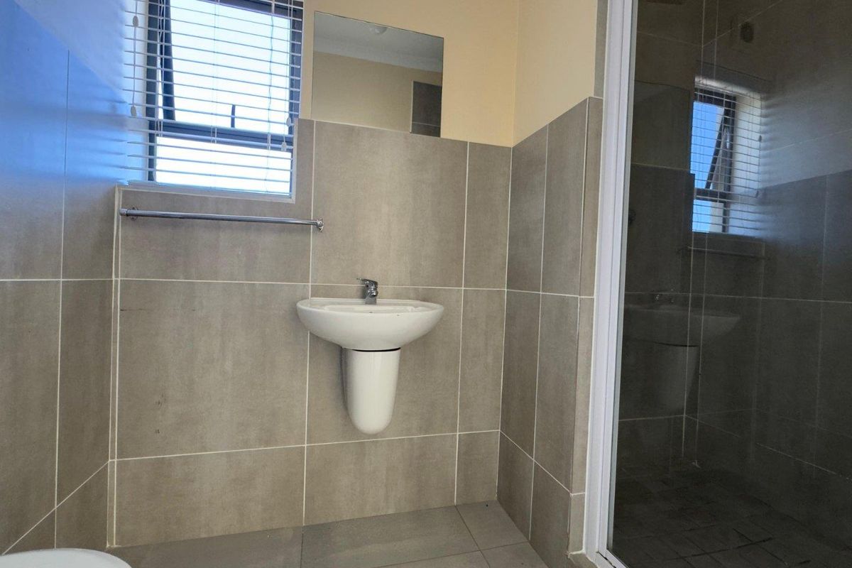 A clean, modern bathroom featuring neutral wall tiles, a pedestal washbasin, and a glass-enclosed shower area.