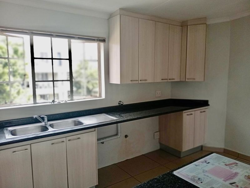 A functional kitchen featuring light wood cabinetry, dark granite countertops, and a double basin sink, with space provided for under-counter appliances.