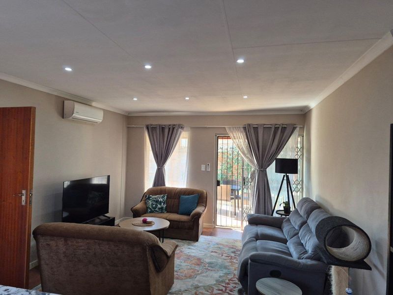 A comfortable living room featuring recessed downlighting, a split-system air conditioner, and direct access to an outdoor patio area through a sliding glass door.