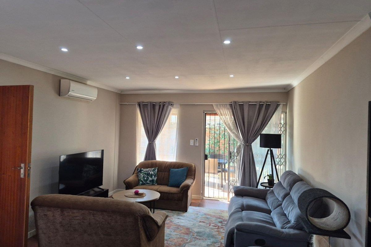 A comfortable living room featuring recessed downlighting, a split-system air conditioner, and direct access to an outdoor patio area through a sliding glass door.