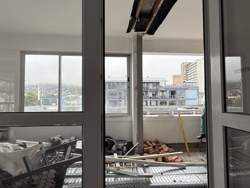 An unfinished balcony area currently under renovation, featuring exposed structural elements and sliding glass door access.