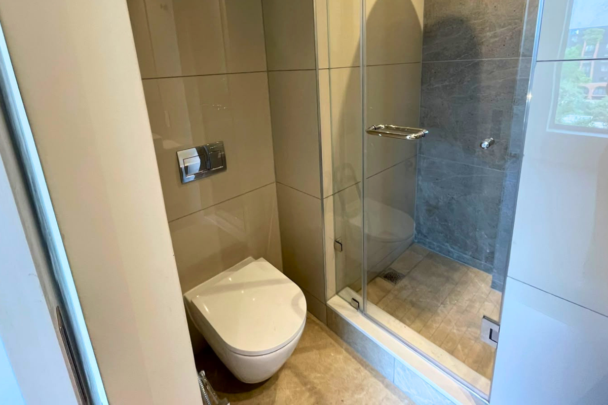 Modern bathroom featuring a wall-hung toilet with a concealed cistern and a glass-enclosed shower with contemporary tiling.