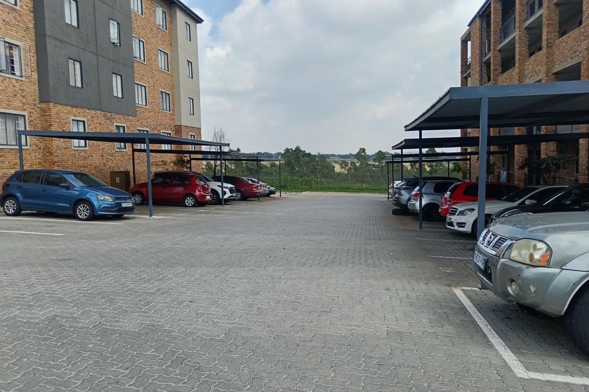 Outdoor parking area featuring paved ground and covered carports situated between apartment building blocks.