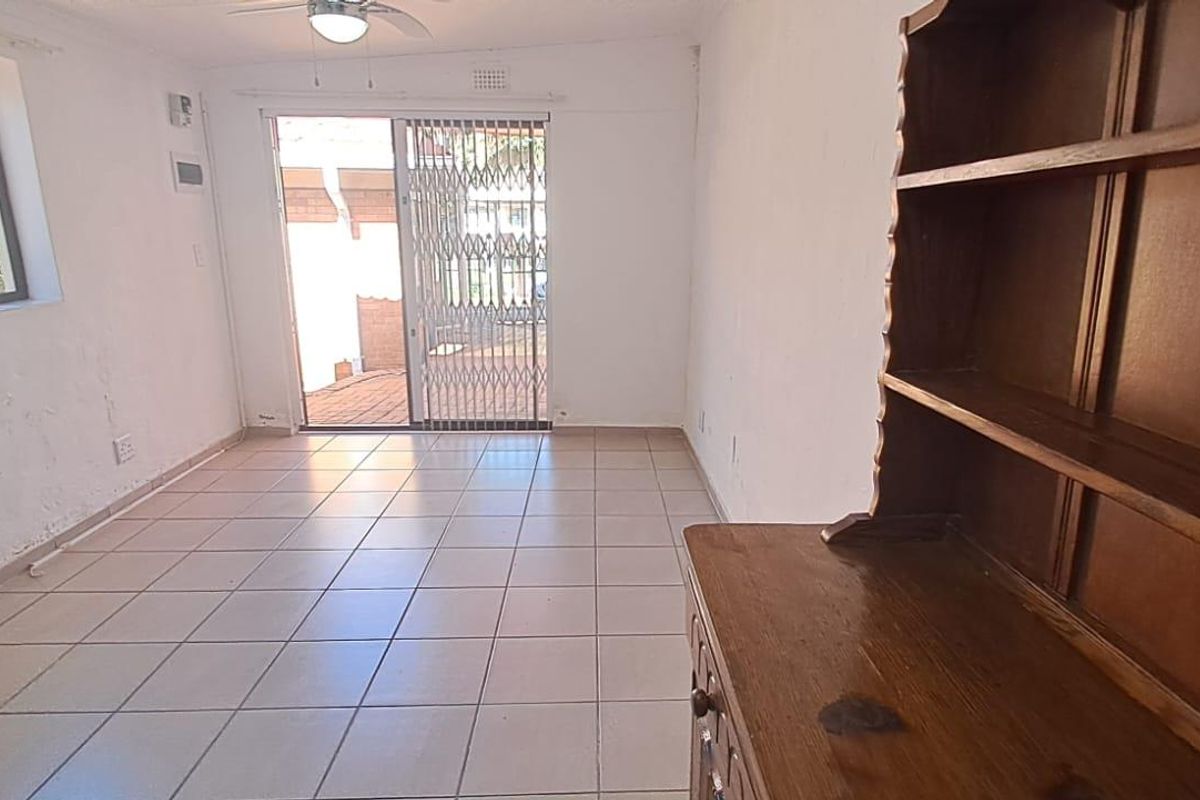 A living room featuring tiled flooring, a ceiling fan, and a sliding door leading to an outdoor area with security gate.