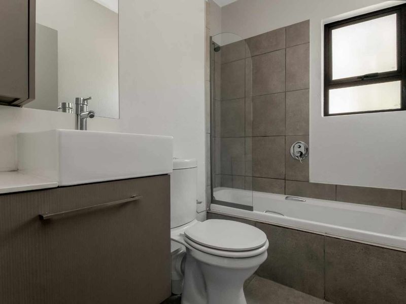 Modern bathroom featuring a vanity with vessel sink, toilet, and a bathtub with a glass shower screen and tiled surround.