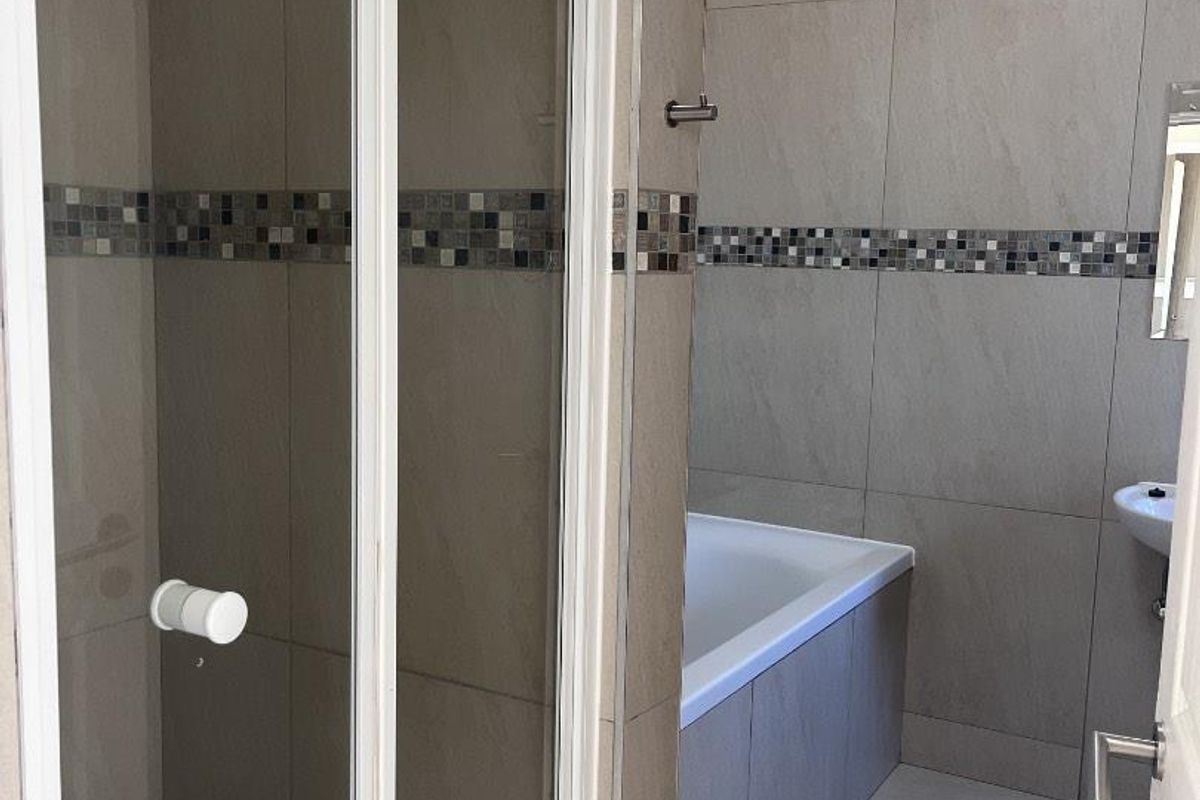 A clean, modern bathroom featuring a glass-enclosed shower, a built-in bathtub, and neutral wall tiles with a decorative mosaic accent border.