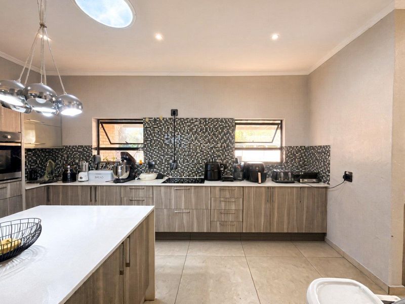 Modern kitchen featuring wood-grain cabinetry, a central island, mosaic tile backsplash, built-in oven, cooktop, and a skylight providing natural light.