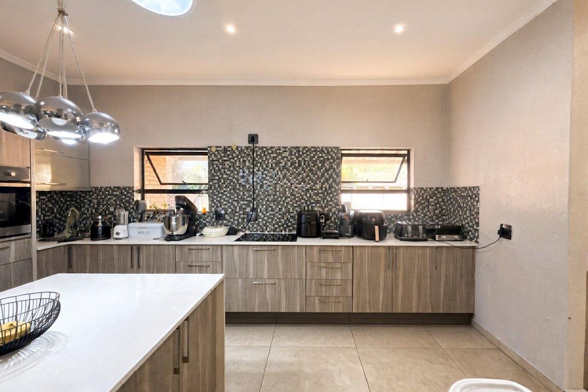 Modern kitchen featuring wood-grain cabinetry, a central island, mosaic tile backsplash, built-in oven, cooktop, and a skylight providing natural light.