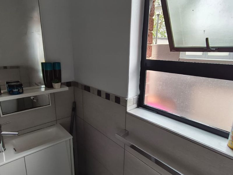 A compact bathroom featuring a modern vanity cabinet with a basin, wall-mounted mirror, and tiled walls, complemented by a functional top-hung window.