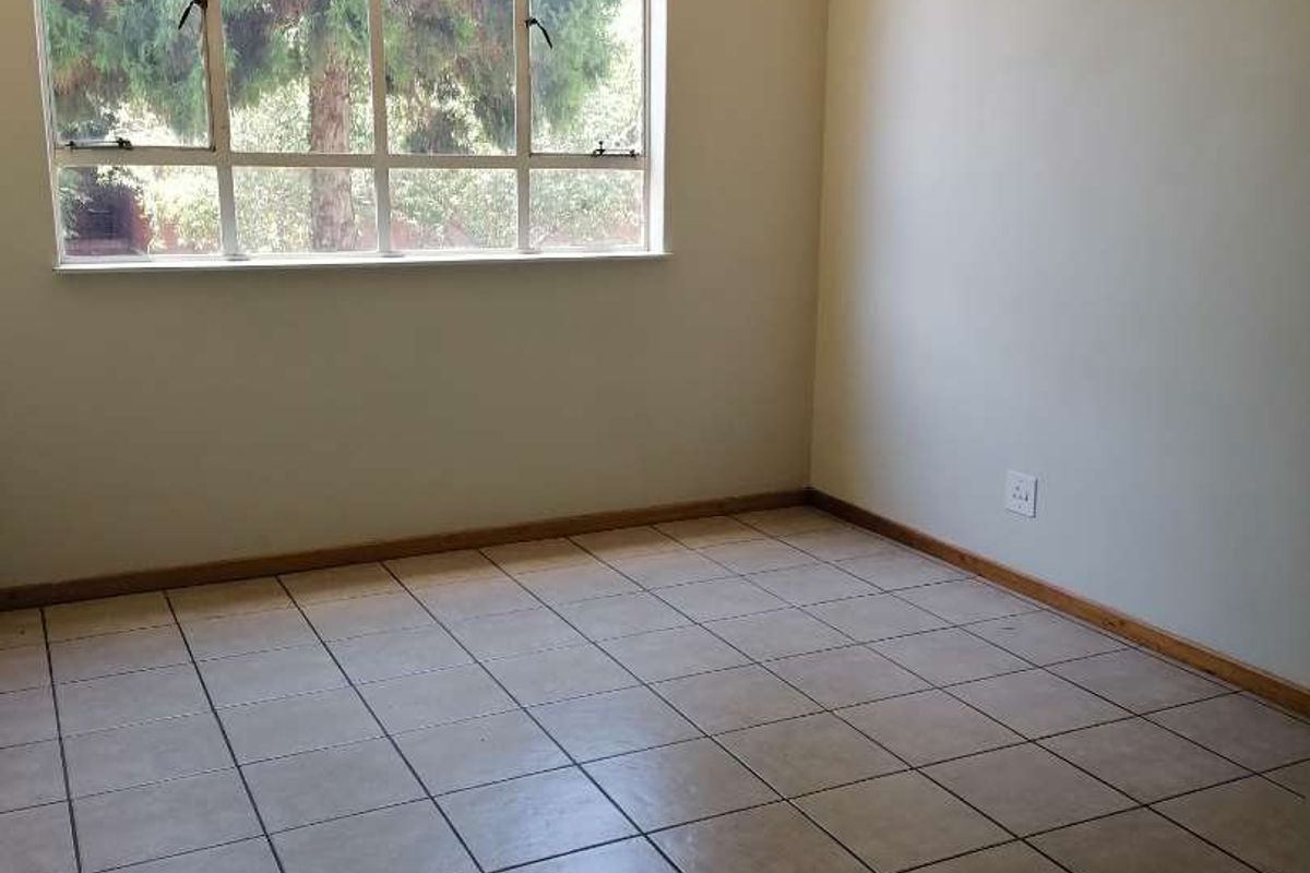 A bright, empty bedroom featuring neutral tiled flooring, a large window providing natural light, and a simple pendant light fixture.