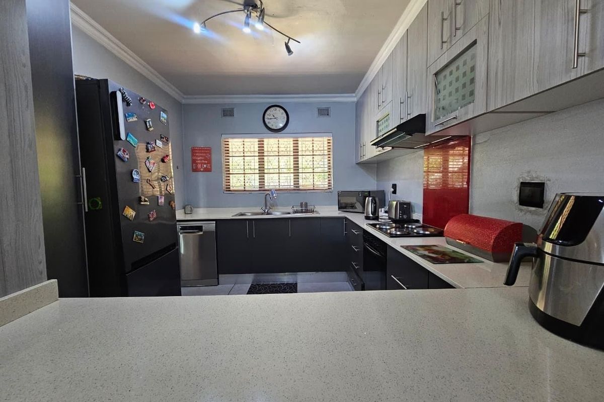 A functional kitchen featuring modern grey cabinetry, stone countertops, integrated appliances, and a red glass splashback, offering a practical layout for daily cooking.