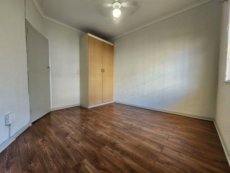 A simple, empty bedroom featuring laminate flooring and a built-in wooden wardrobe, offering a clean canvas for personalization.