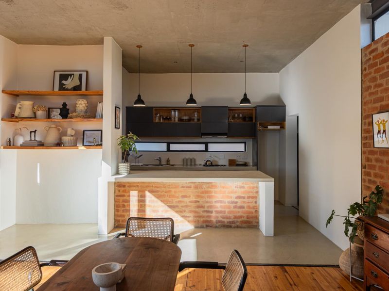 Modern open-plan kitchen featuring exposed concrete ceilings, brick accents, and a central island, seamlessly integrated into the living space.