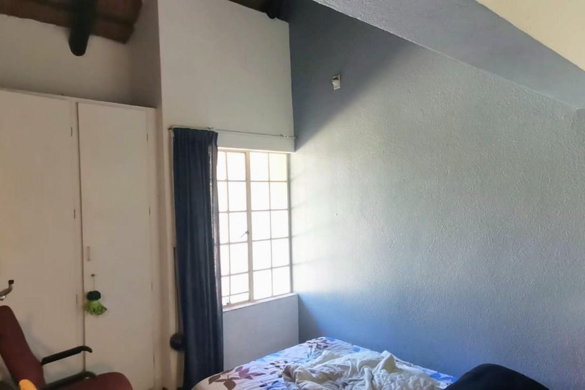 A bedroom featuring exposed timber ceiling beams, a built-in wardrobe, and a grid-pattern window allowing natural light.