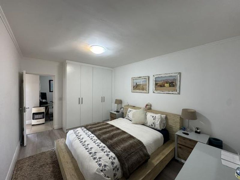 A well-maintained bedroom featuring built-in cupboards, laminate flooring, and neutral finishes, with an adjoining room visible through the doorway.